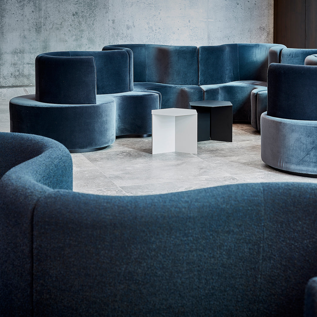 Velvet seating in deep blue tones with curved shapes, complemented by minimalist white and black accent tables.