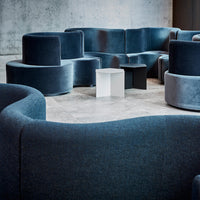Velvet seating in deep blue tones with curved shapes, complemented by minimalist white and black accent tables.