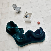 Teal velvet sofa with organic curves, paired with a grey upholstered chair, on a light tile floor.