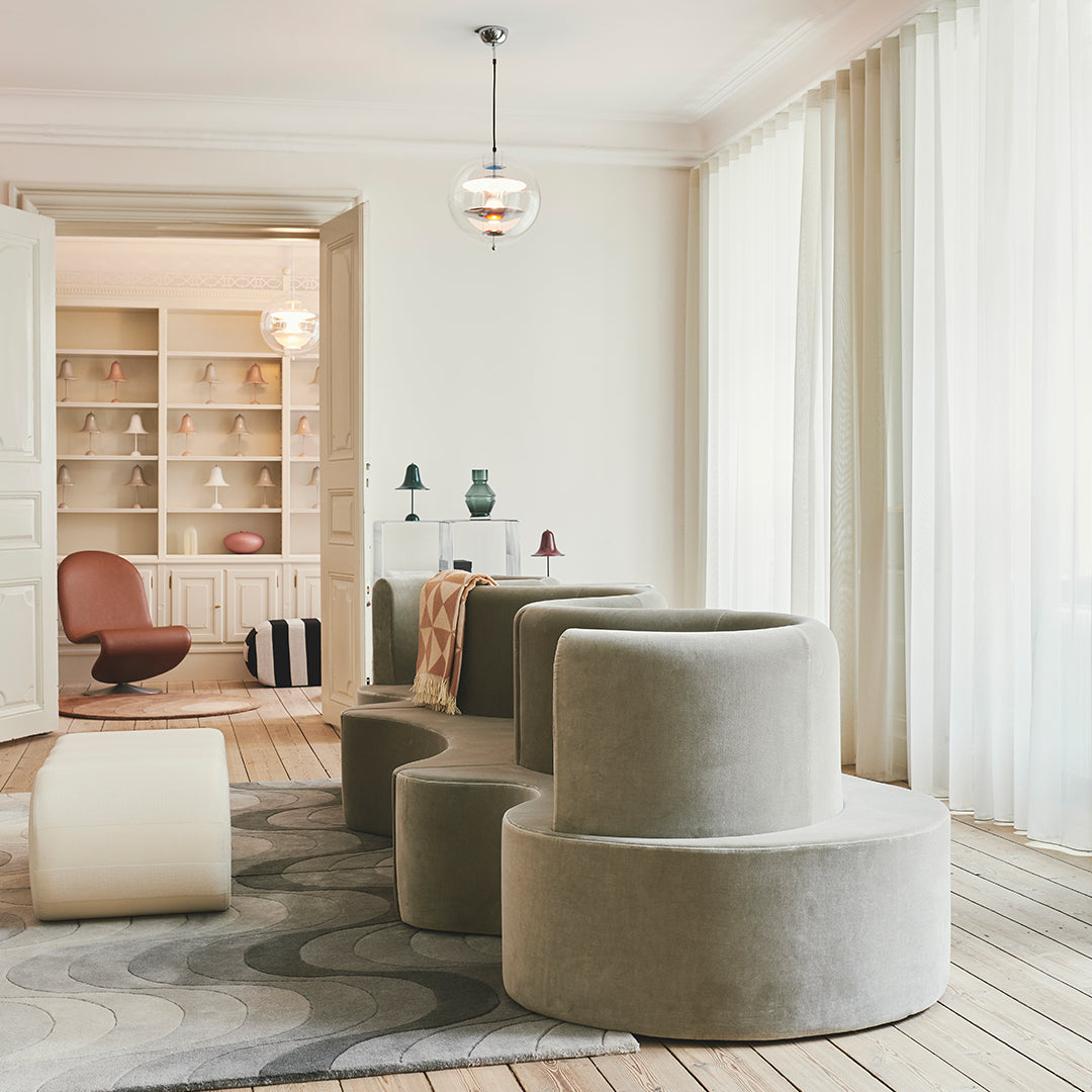 Stylish gray curved seating with warm accents and a soft wave-patterned rug in a bright, airy setting.
