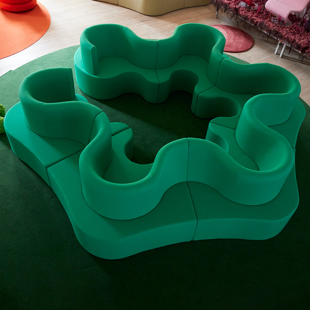 Curvy green modular seating on a dark green carpet, featuring a bold, playful design.