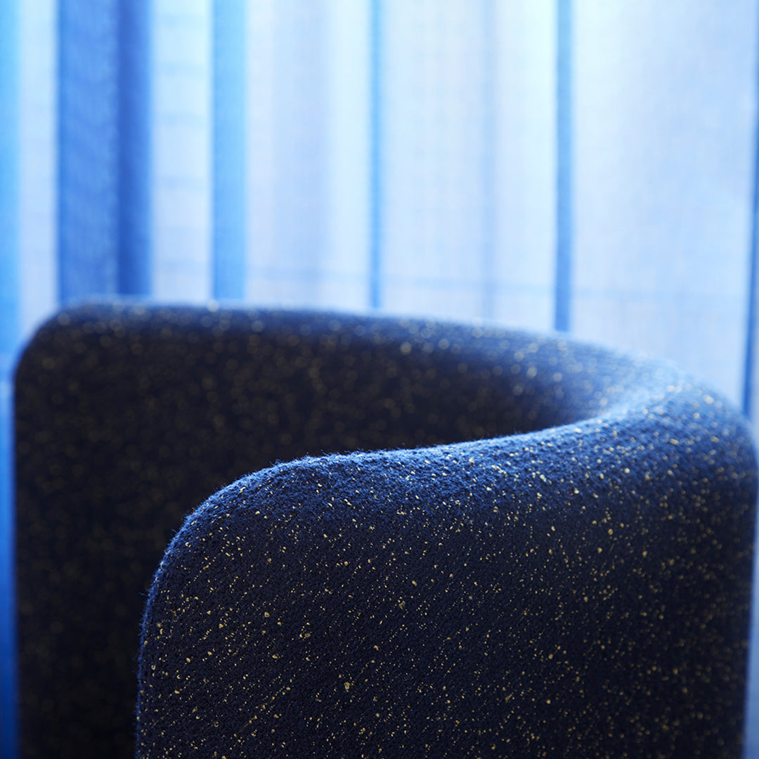 Close-up of a dark blue textured fabric with subtle golden flecks against a soft blue background.