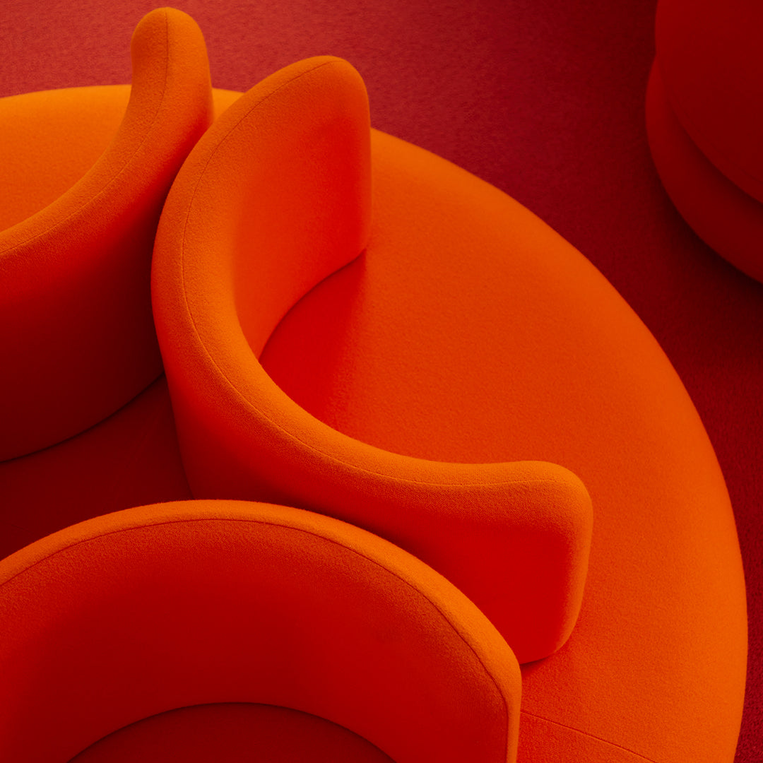 Vibrant orange circular seating with smooth, soft curves on a textured red background.