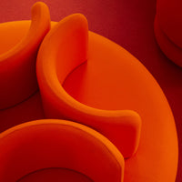 Vibrant orange circular seating with smooth, soft curves on a textured red background.