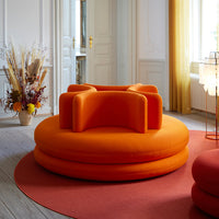 Bright orange circular sofa with bold, rounded shapes, complemented by a soft red rug in a stylish interior.