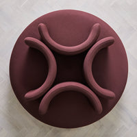 Burgundy fabric circular seating with smooth, curved armrests on a light wood floor.
