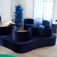 Navy velvet modular sofa with rounded shapes, complemented by blue floral decor and light wooden flooring.
