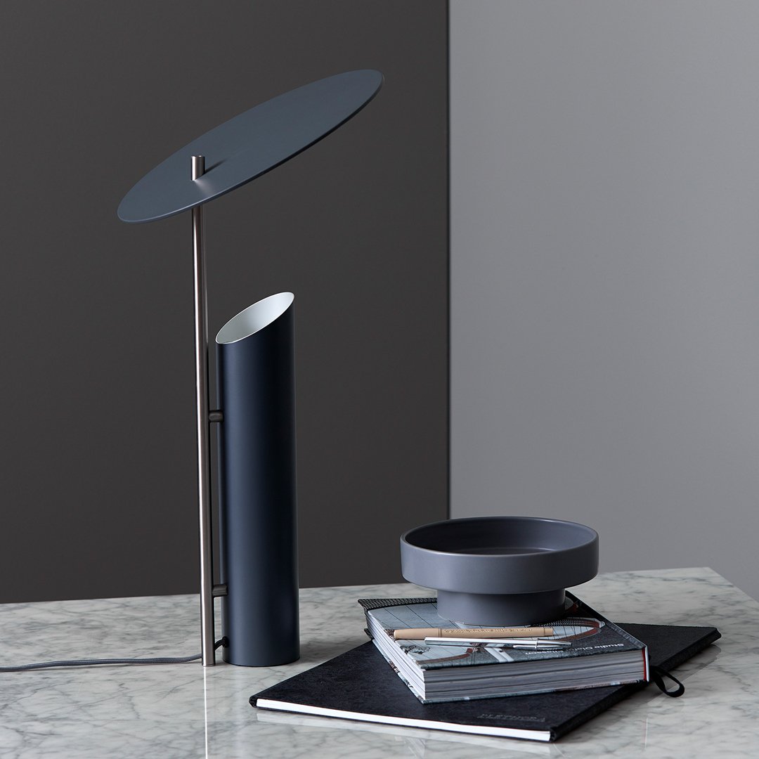 Modern blue lamp with circular shade, complemented by a sleek grey bowl and patterned black notebook on a marble surface.