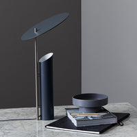 Modern blue lamp with circular shade, complemented by a sleek grey bowl and patterned black notebook on a marble surface.