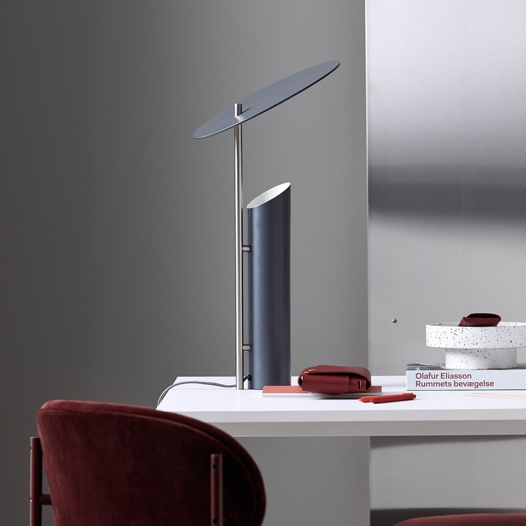 Sleek gray desk lamp with a circular shade, paired with deep red upholstery and minimalist white decor.