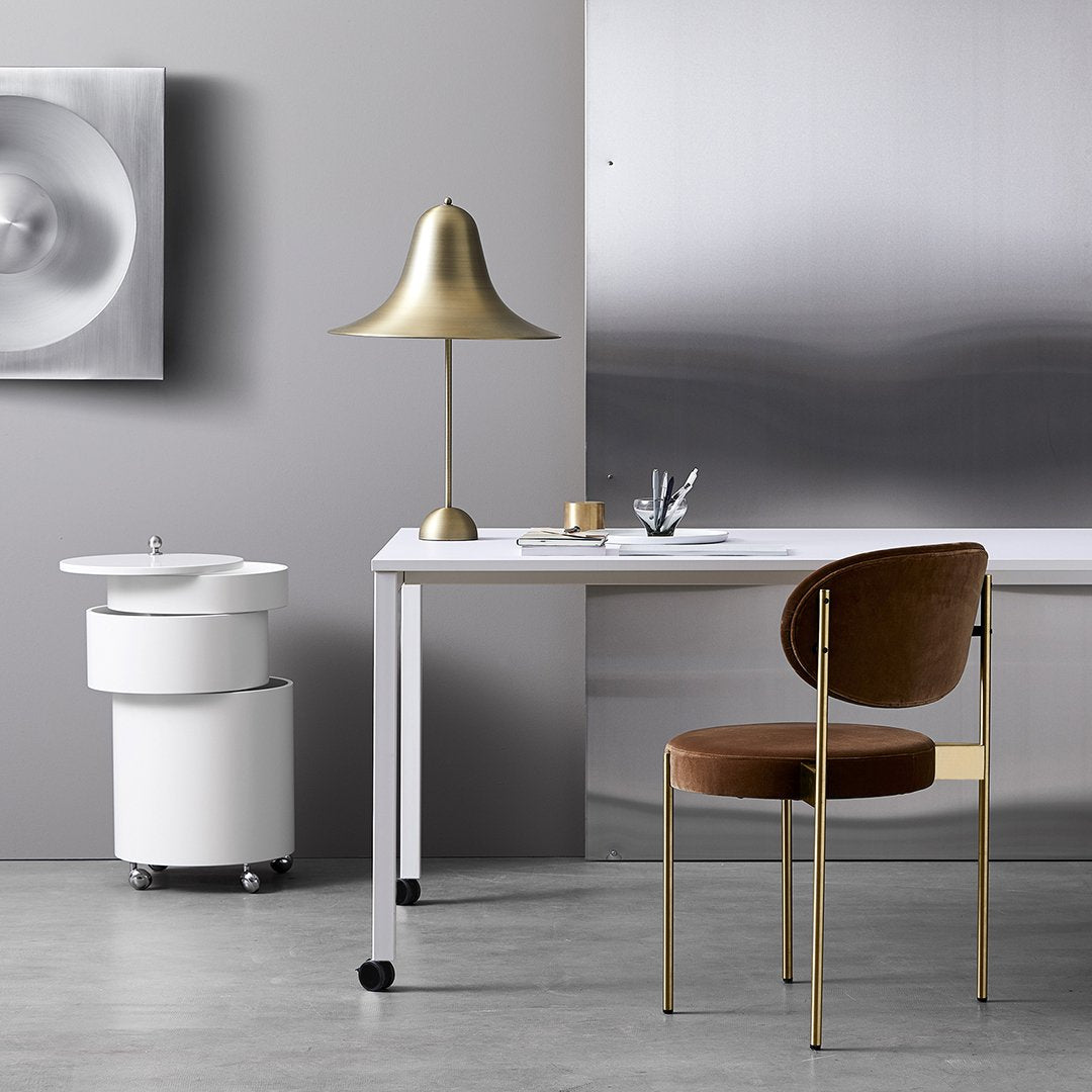 Modern workspace featuring a brass lamp, white desk, brown velvet chair, and sleek metal accents in a neutral color palette.