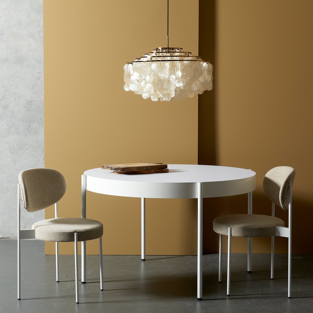 Round white dining table with beige upholstered chairs, accented by a soft, neutral-toned wall. Elegant and modern design.