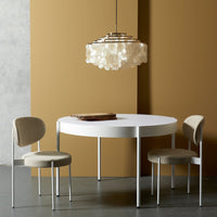 Round white dining table with beige upholstered chairs, accented by a soft, neutral-toned wall. Elegant and modern design.