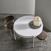 Round white dining table with gray velvet chairs, minimalist design, soft colors, and smooth textures.