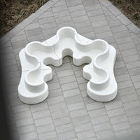 White abstract seating design with smooth curves on a gray paved surface. Modern and minimalist aesthetic.