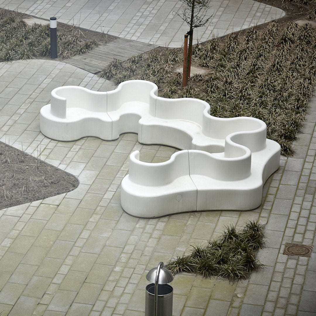 Stylish white abstract bench with an organic shape, set against a textured gray pathway and green grass.