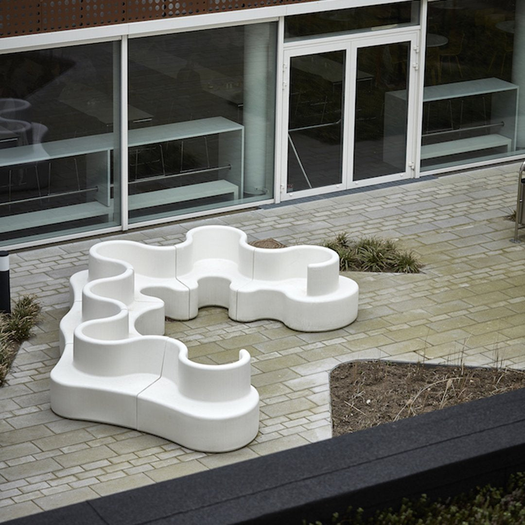 Modern white outdoor sectional sofa with fluid, organic shapes, set against a paved patio and greenery.
