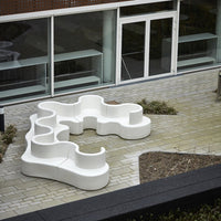 Modern white outdoor sectional sofa with fluid, organic shapes, set against a paved patio and greenery.