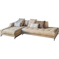 Beige suede sectional sofa with tufted cushions and assorted patterned decorative pillows in soft neutral tones.