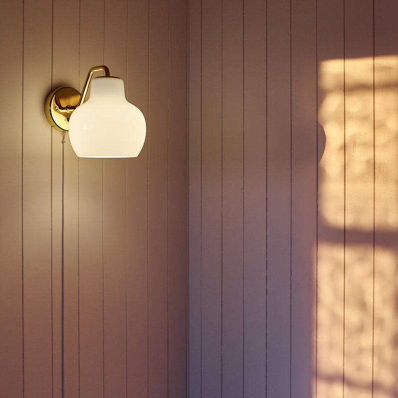 Elegant white glass wall lamp with a gold fixture casting soft light and a warm shadow on textured beige paneling.