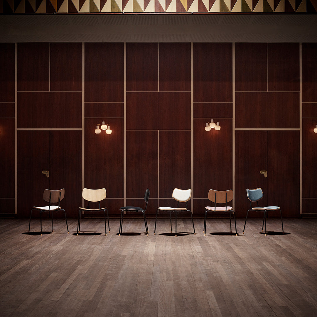 Various minimalist chairs in black, white, natural wood, and light blue against a brown wood panel backdrop.