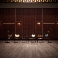 Various minimalist chairs in black, white, natural wood, and light blue against a brown wood panel backdrop.