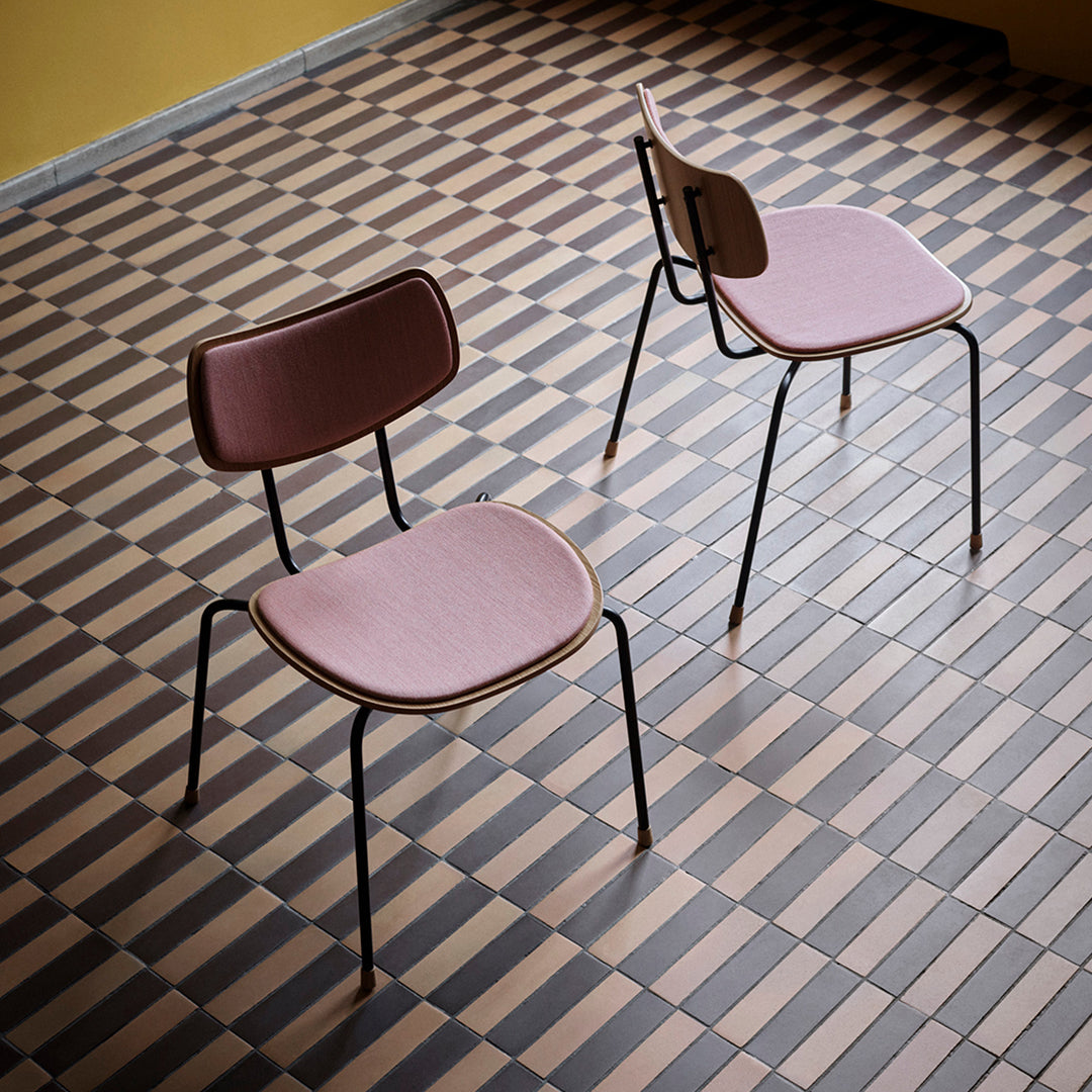 "Two pink upholstered chairs on a checkered brown and beige tile floor."
