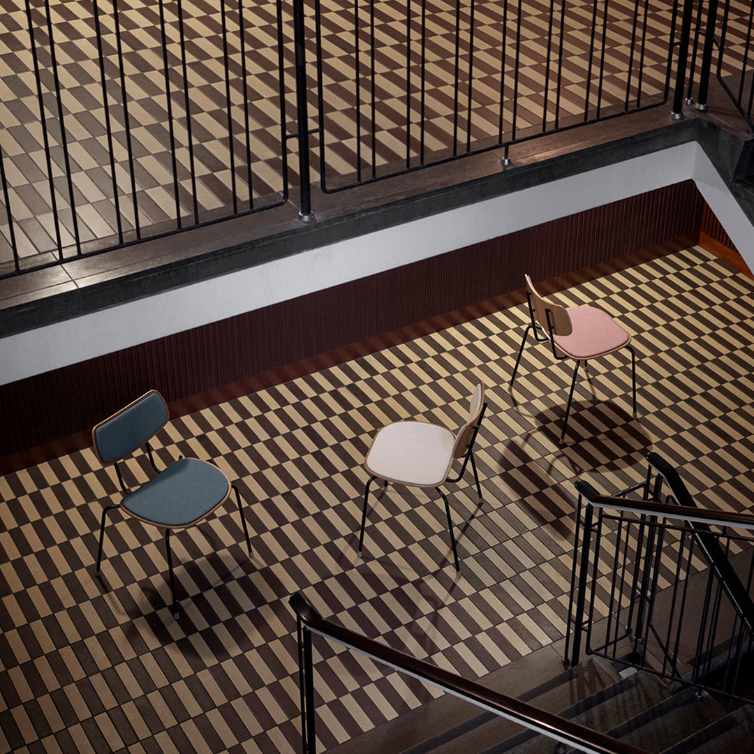 Three colorful chairs in blue, white, and pink on a patterned brown and beige floor. Modern design elements.