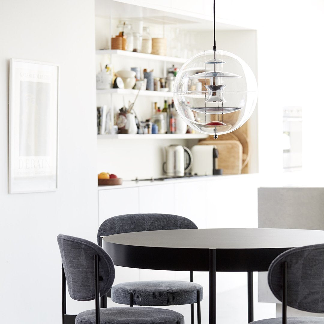 Round black dining table with gray upholstered chairs, featuring a modern and minimalist aesthetic in a bright space.
