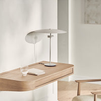 Modern wooden desk in light oak with soft beige accents and a sleek white lamp, showcasing minimalist design.