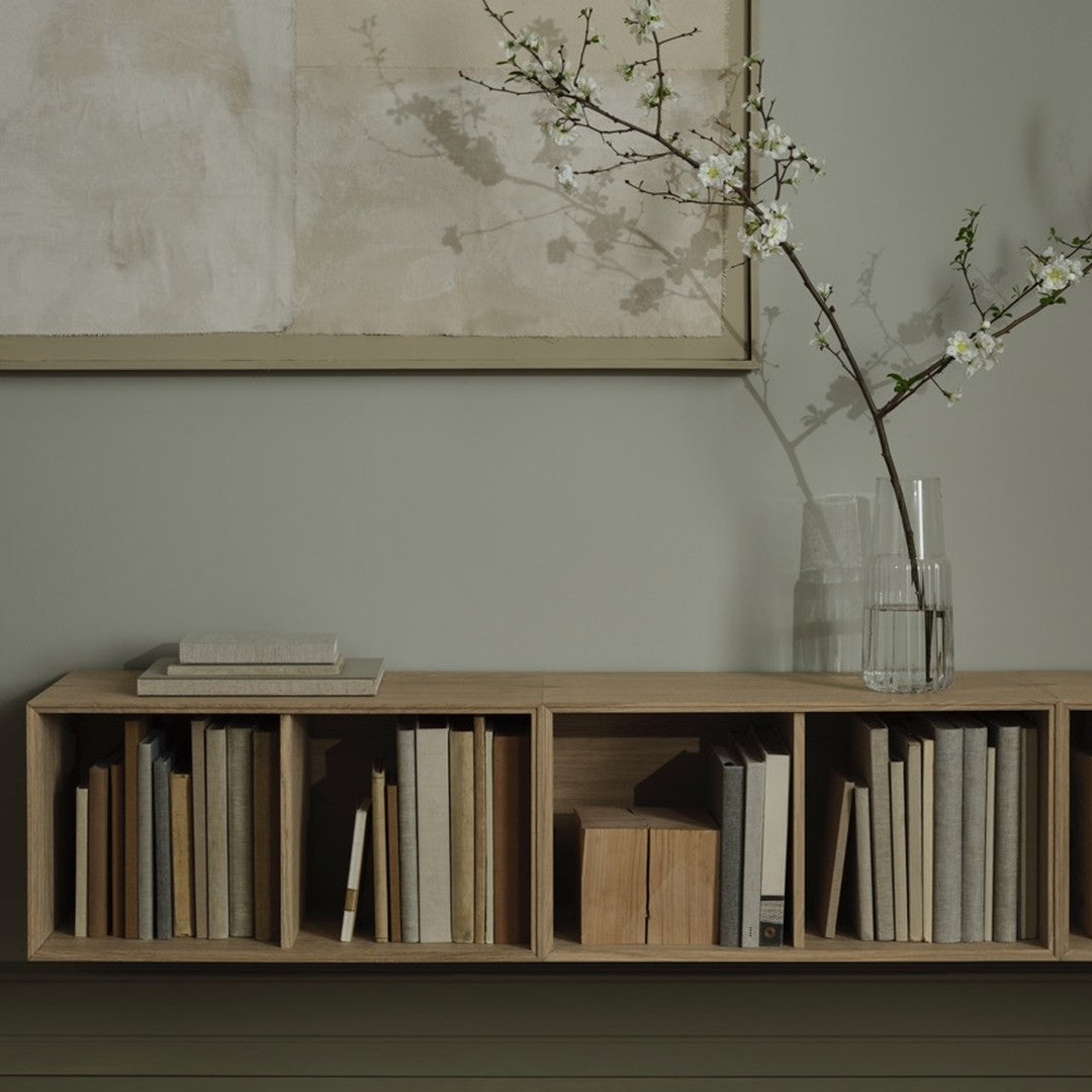 Light wood bookshelf with neutral-colored books, soft beige wall, and minimalist floral decor for a modern aesthetic.