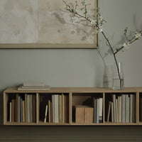 Neutral tones and light wood grain in a minimalist bookshelf with organized books, complemented by soft green walls.