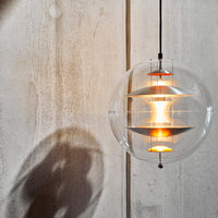 Clear glass pendant light with warm orange accents and layered white patterns, casting soft shadows on a concrete background.