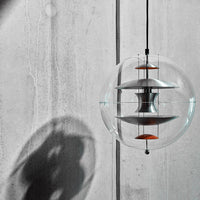 Modern glass pendant light with layered silver and orange accents, casting dramatic shadows on a concrete wall.
