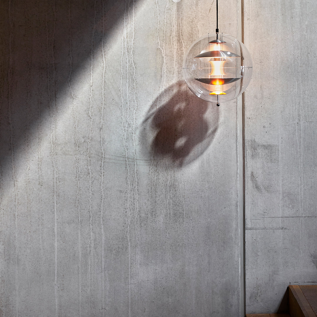 Clear globe pendant light casting a circular shadow on a textured gray wall, featuring warm amber illumination.