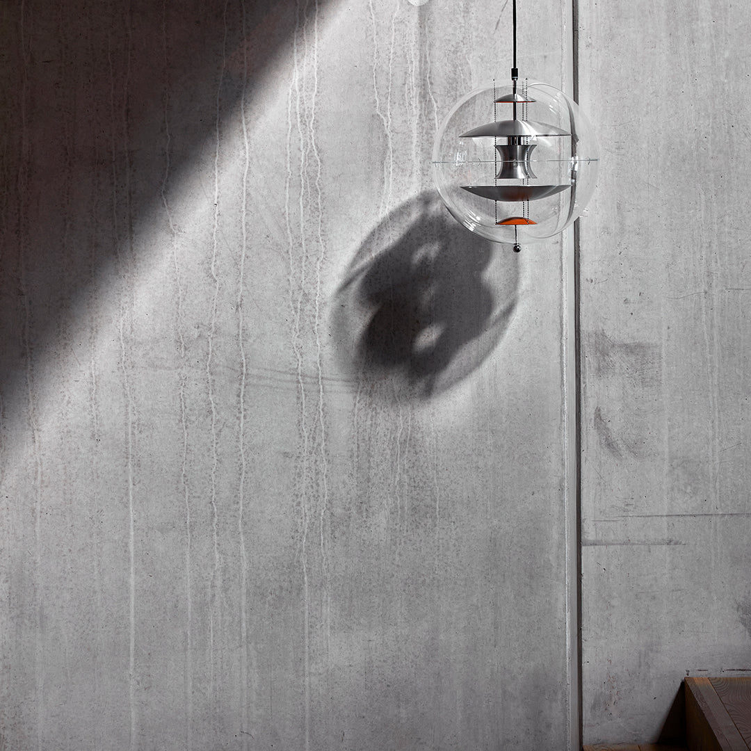 Clear glass pendant light casting a soft shadow on a textured gray concrete wall. Minimalist design with modern aesthetics.