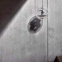 Clear glass pendant light casting a soft shadow on a textured gray concrete wall. Minimalist design with modern aesthetics.