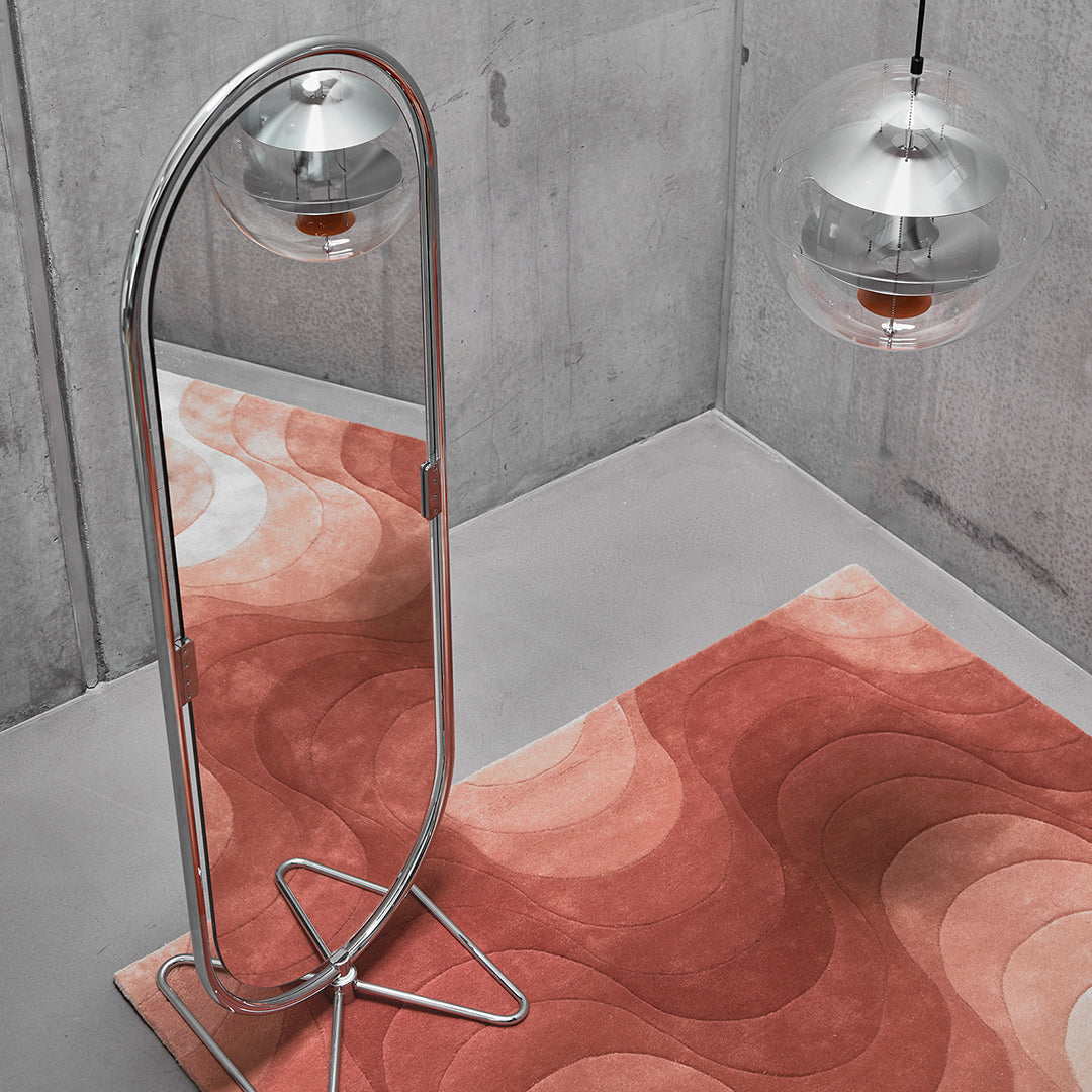 Curvy orange and pink patterns on a plush rug beneath a sleek silver mirror and modern pendant lights.