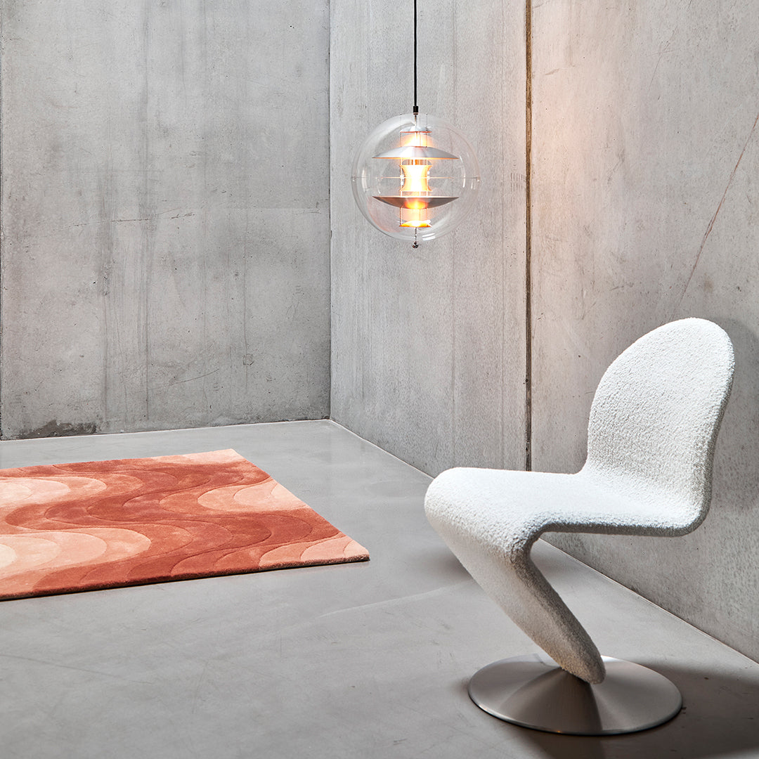 White modern chair with a curved design next to an orange circular patterned rug in a minimalist concrete setting.