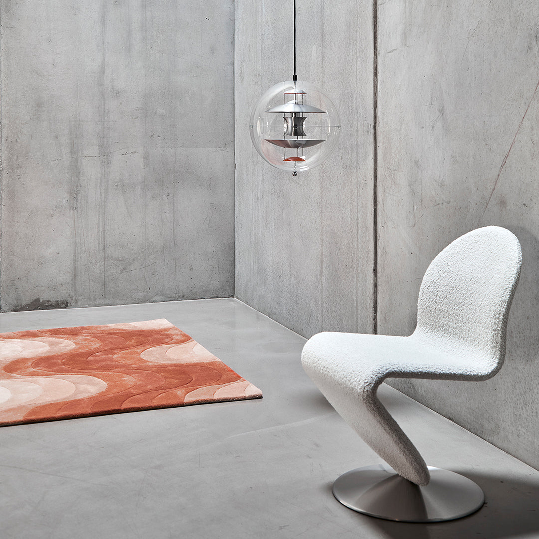 White curve chair, orange circular pattern rug, gray concrete wall and floor, modern minimalist decor.