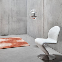 White curve chair, orange circular pattern rug, gray concrete wall and floor, modern minimalist decor.