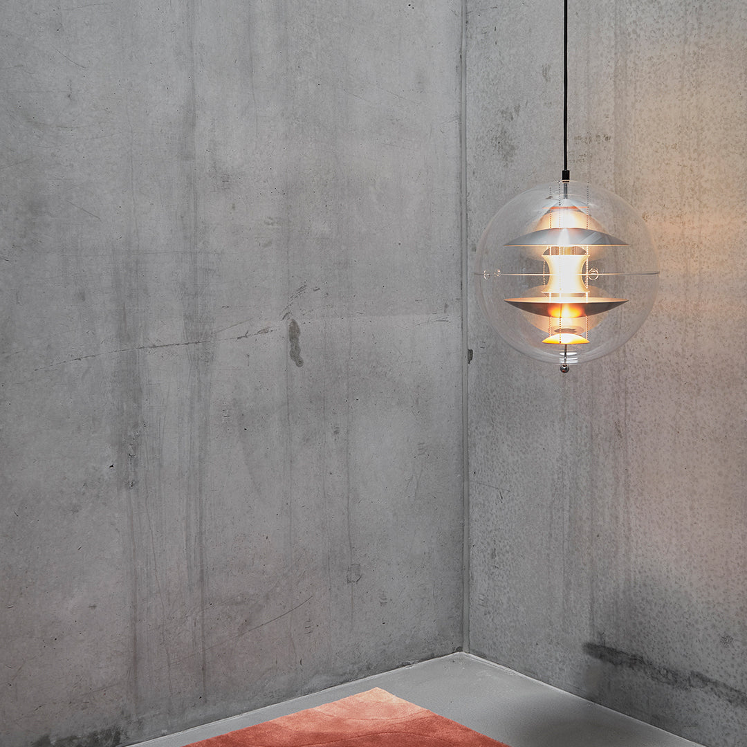 Modern pendant light featuring a clear globe design, warm yellow glow, and minimalist gray concrete backdrop.