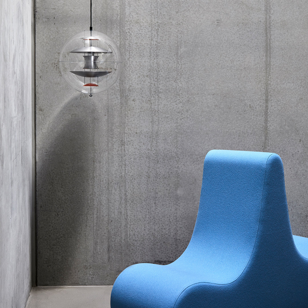 "Modern blue chair against a textured concrete wall, featuring a clear pendant light for a sleek aesthetic."
