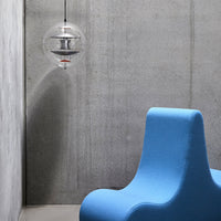 "Modern blue chair against a textured concrete wall, featuring a clear pendant light for a sleek aesthetic."