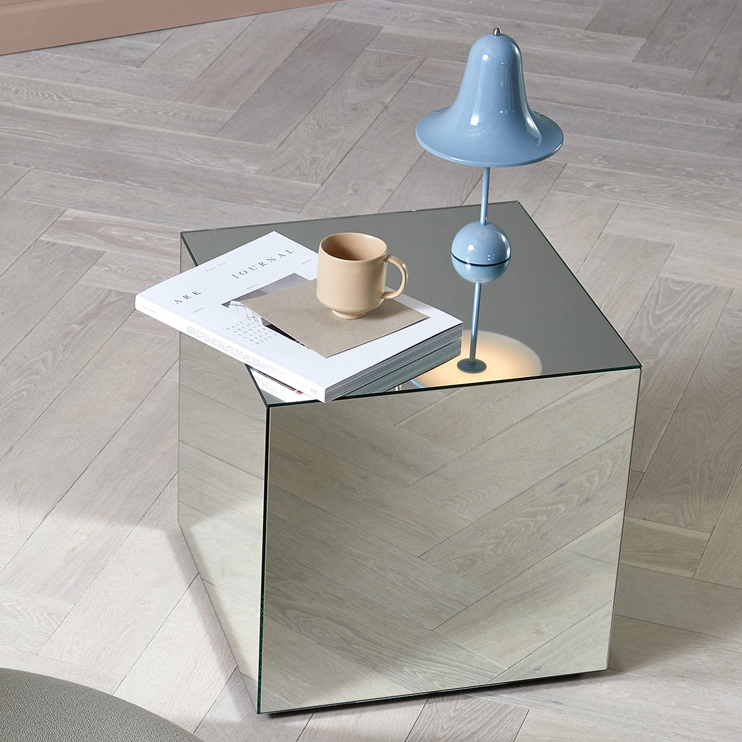 Reflective cube side table with sleek mirrored surface, featuring a light blue lamp and neutral-toned decor.
