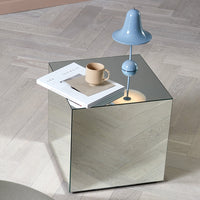 Reflective cube side table with sleek mirrored surface, featuring a light blue lamp and neutral-toned decor.