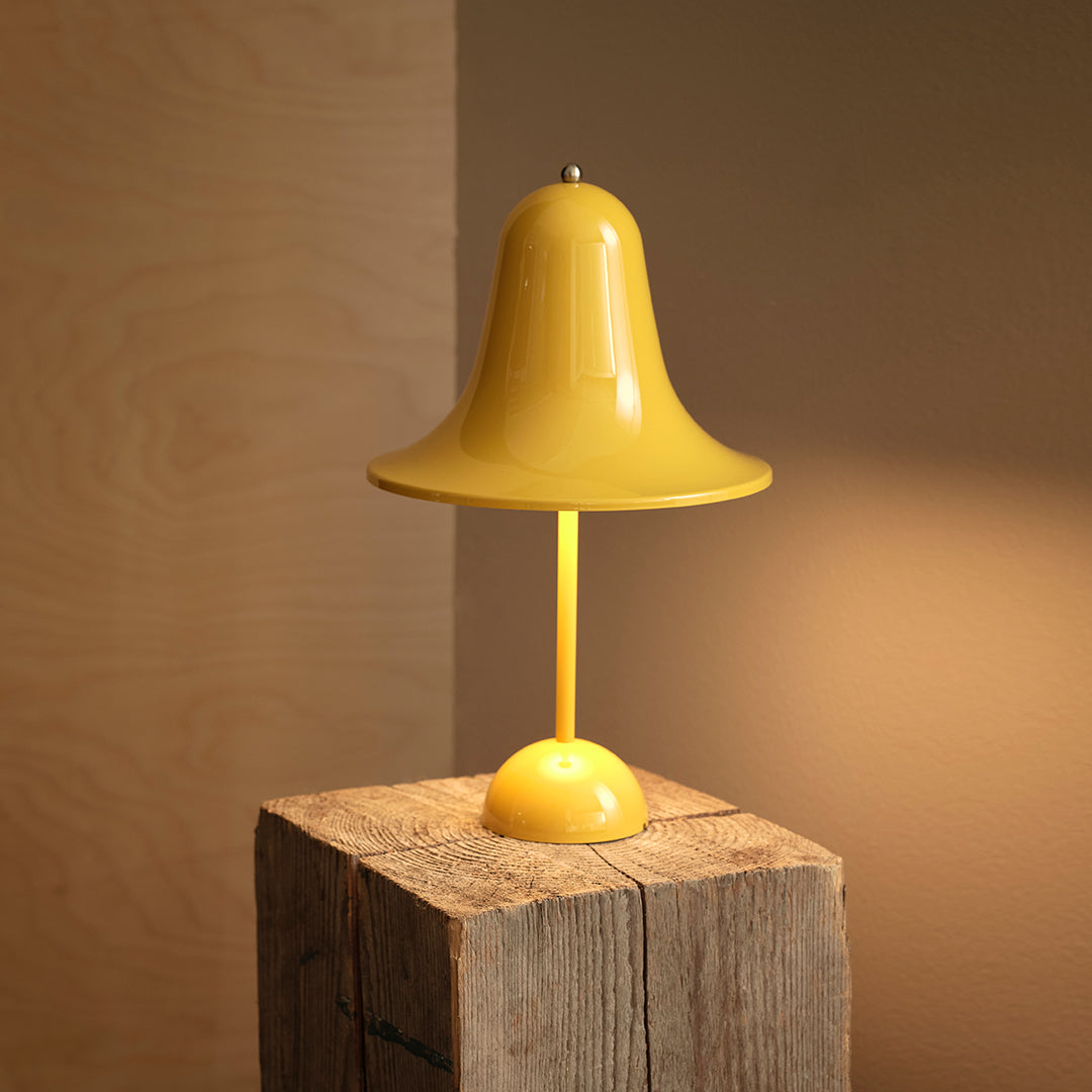 Bright yellow table lamp with a sleek bell shape and smooth finish, set against a natural wood background.