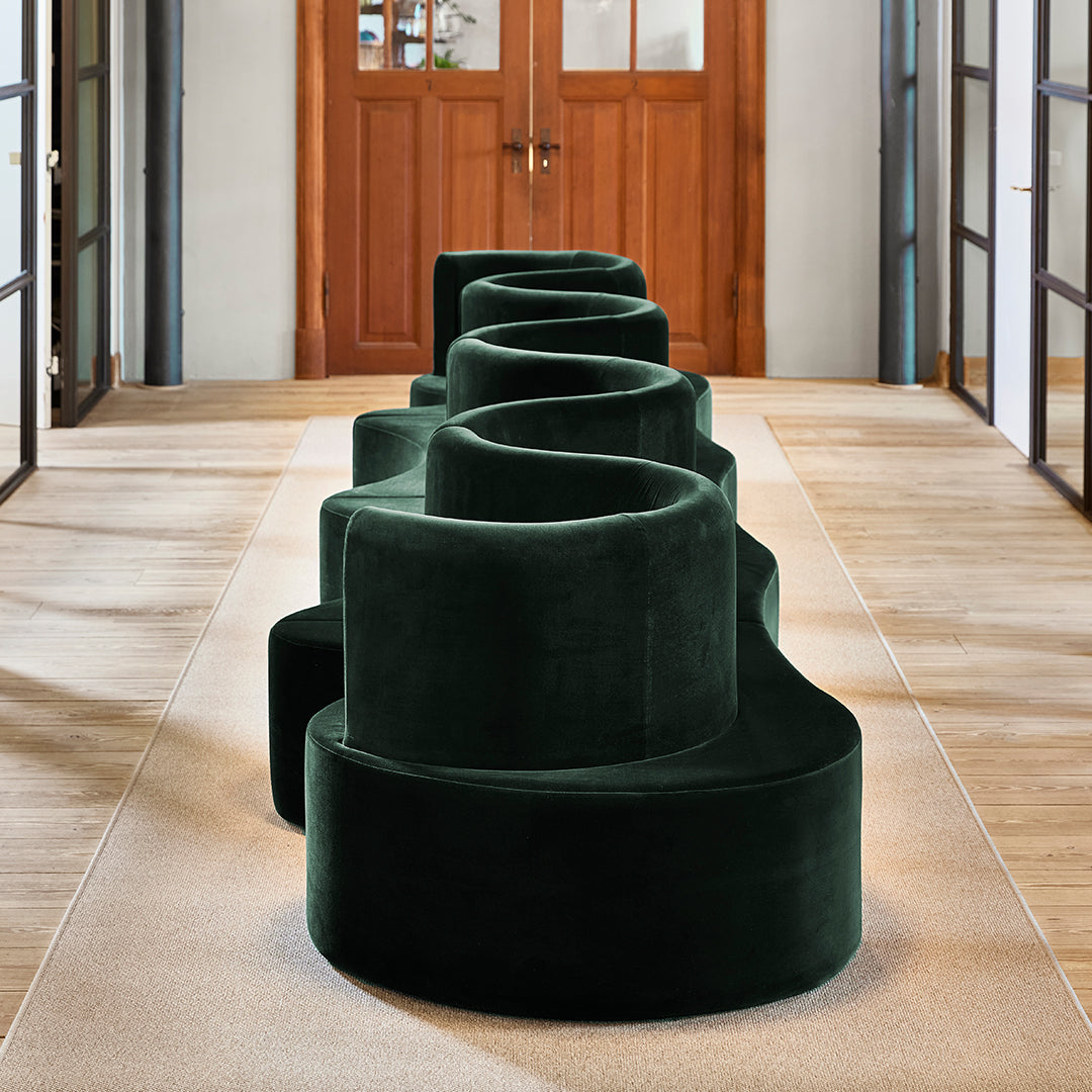 Curved green velvet seating with a soft texture, featuring deep emerald tones and a modern, sculptural design.