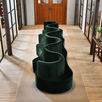 Luxurious dark green velvet sofa with a unique, wavy design, positioned on a neutral-toned rug in a stylish interior.