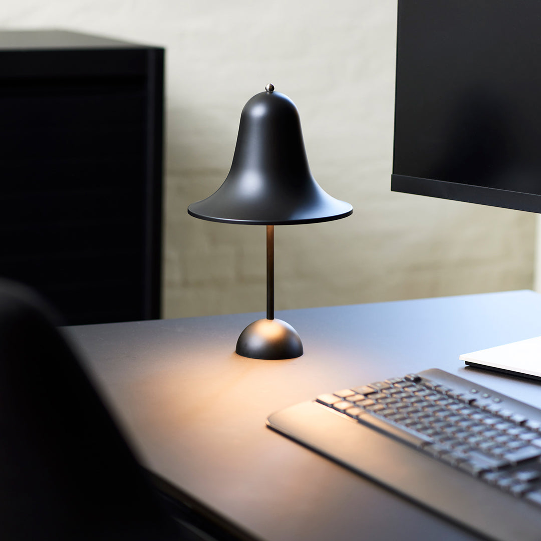 Black bell-shaped table lamp on a sleek dark surface, casting a warm glow with a minimalist design.